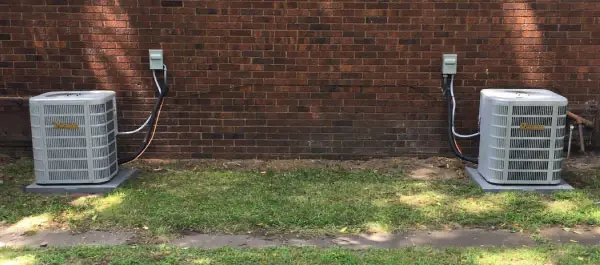 Two new air conditioners installed behind a brick home
